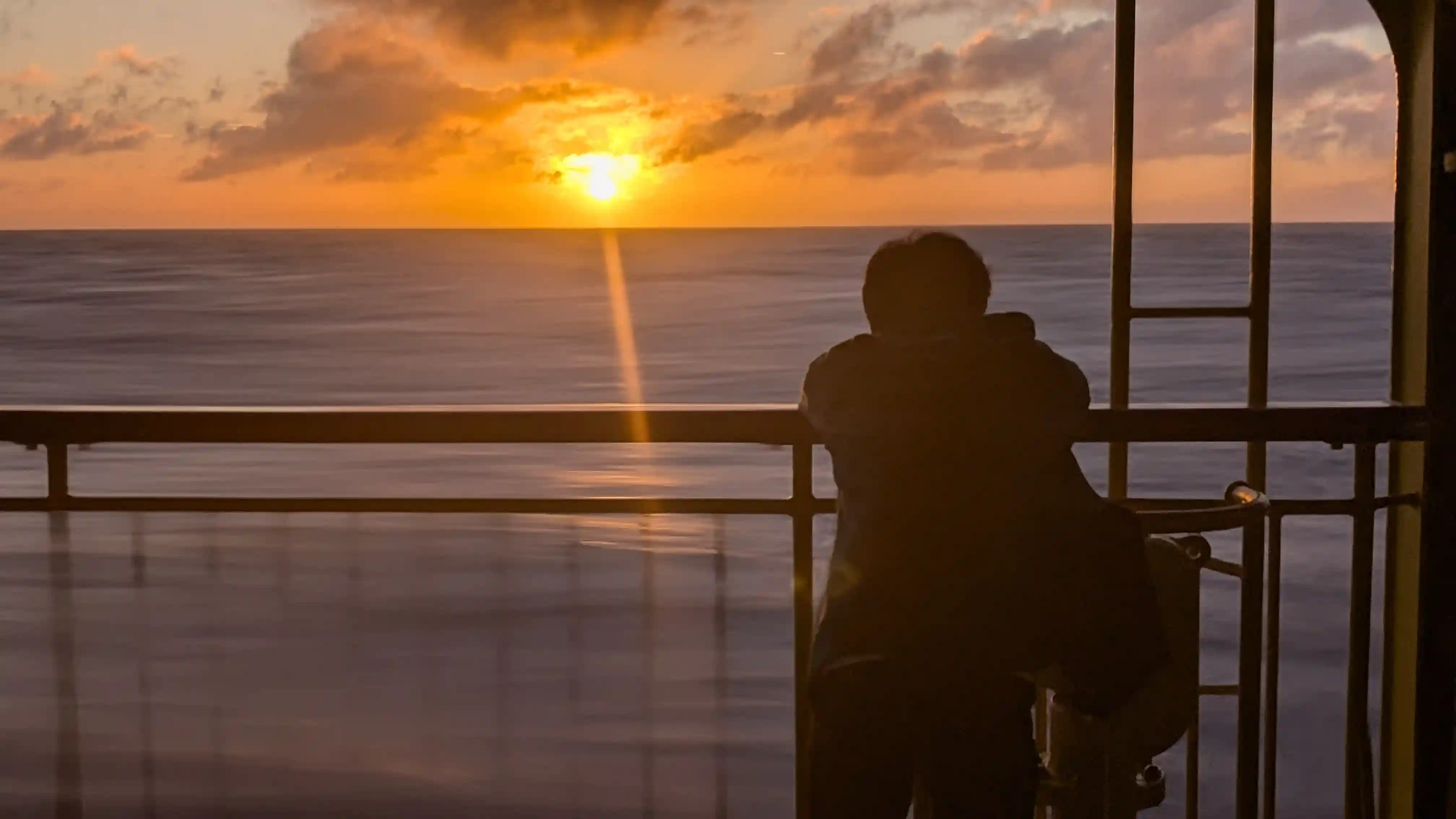 八丈島へのフェリーから見た日の出。柵に人が寄りかかって朝日を眺めている画像。